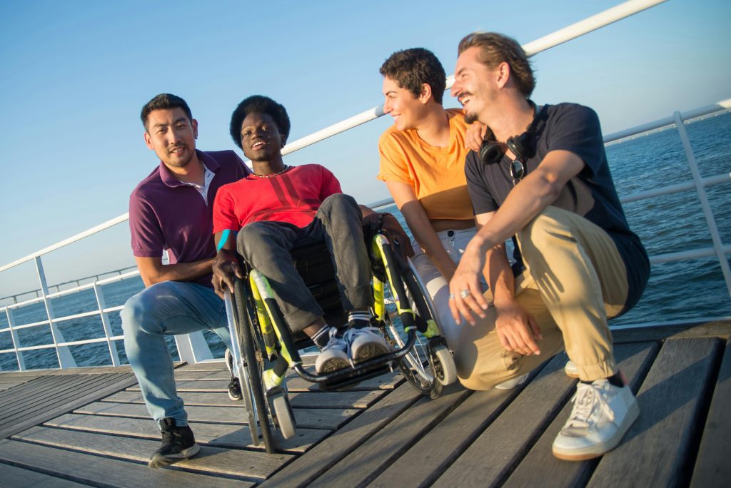 A group of diverse friends enjoying leisure time on a boardwalk by the sea, showcasing camaraderie and inclusivity.